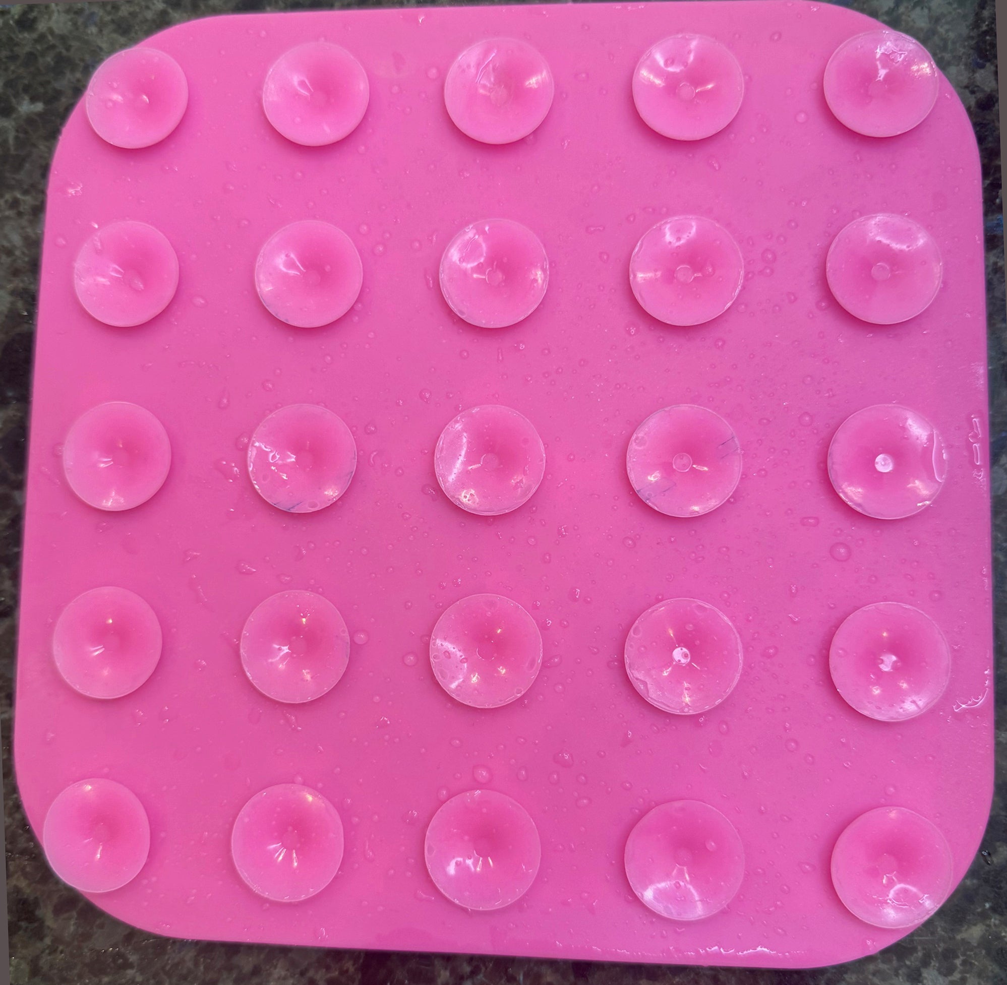 Pink silicone mold with circular cavities on a dark surface