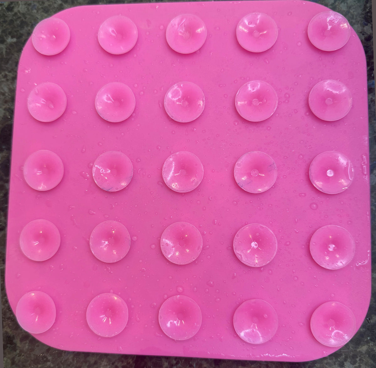 Pink silicone mold with circular cavities on a dark surface